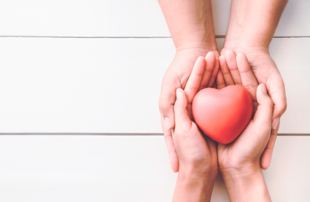 Two pairs of hands overlapped and holding heart